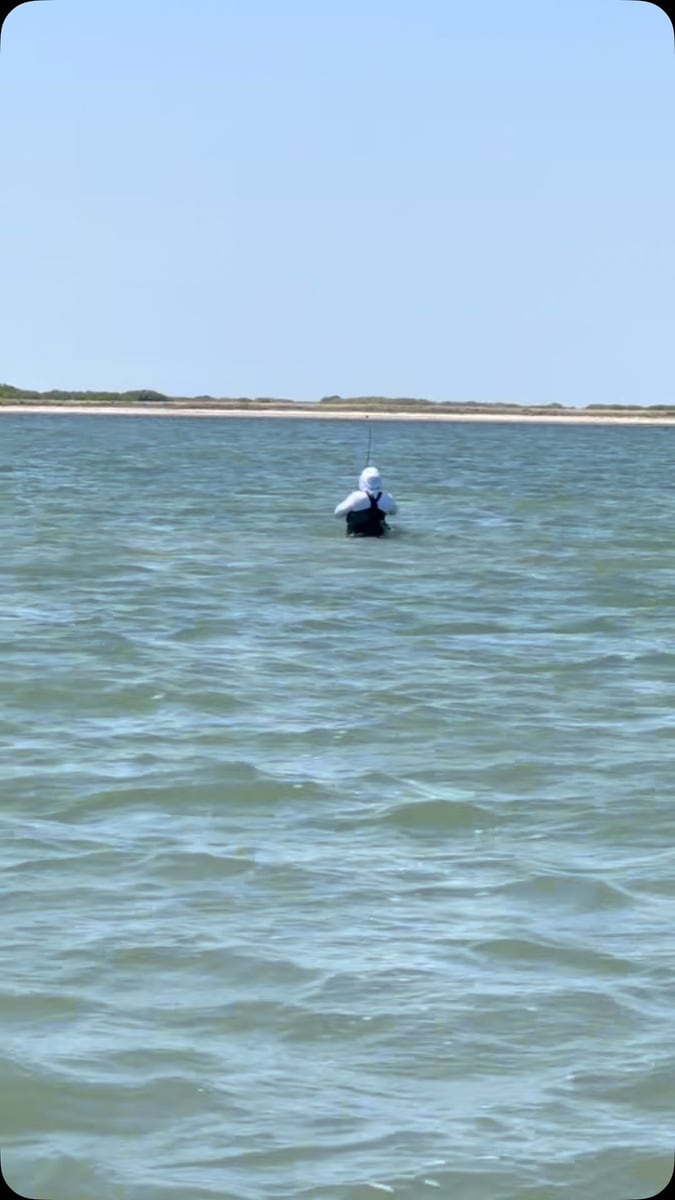 A lone angler wade fishing a wide, shallow coastal flat